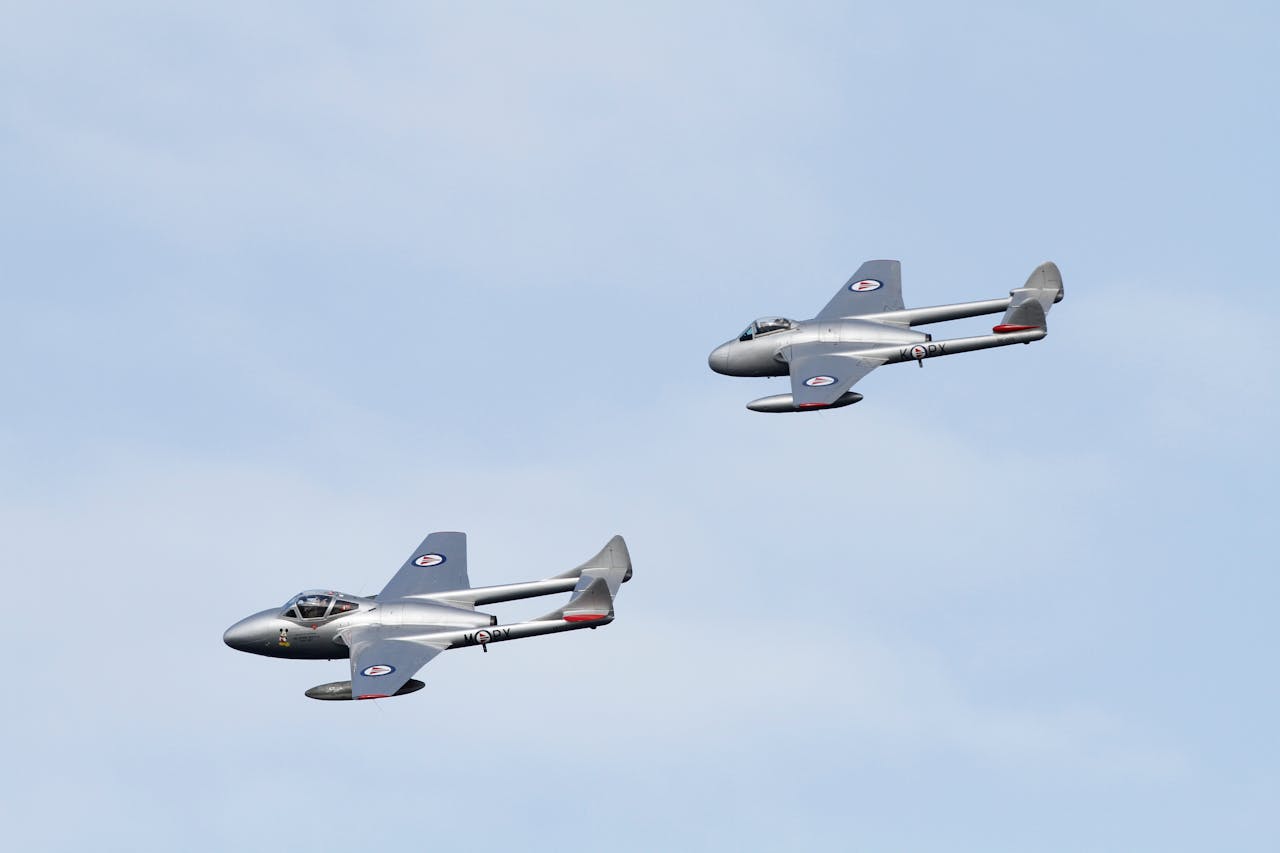 services-03 Two vintage fighter jets fly in formation under a clear blue sky.