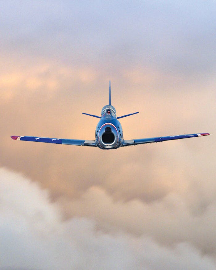 services-01 A vintage F-86 Sabre jet aircraft flies smoothly above clouds during a vibrant sunset.